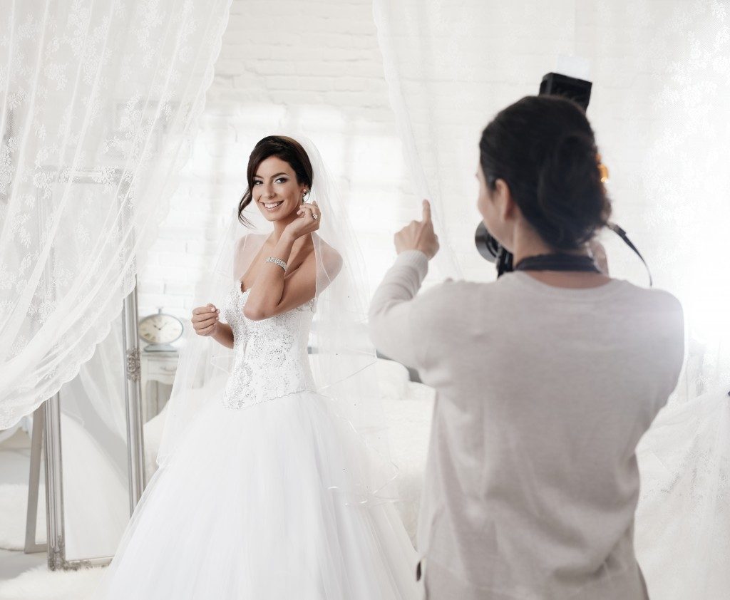 Female photographer photographing beautiful happy bride indoors