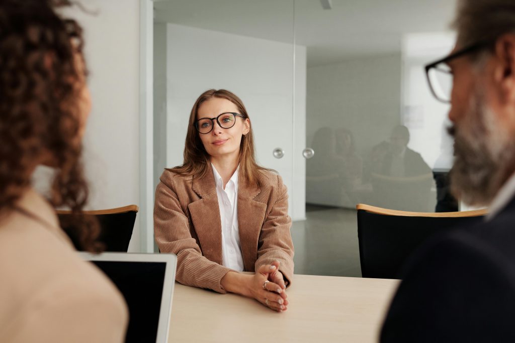 smiling woman with glasses facing a panel of interviewers during a job interview