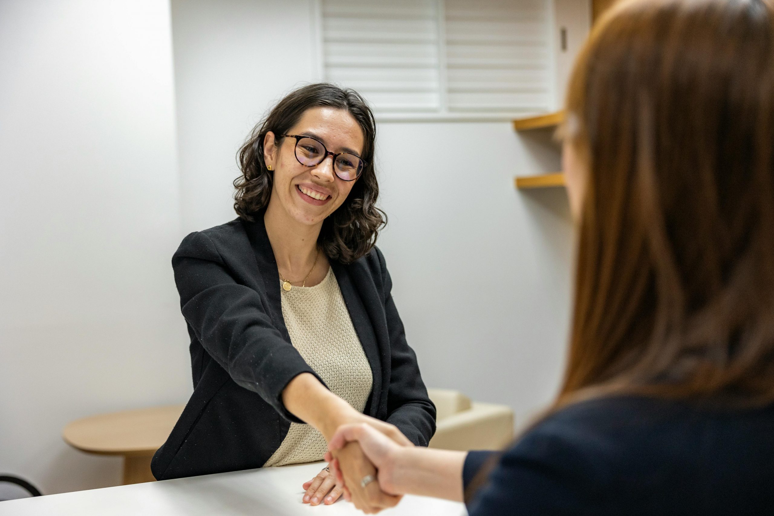 female interviewee with glasses smiling confidently and shaking hands with the interviewer